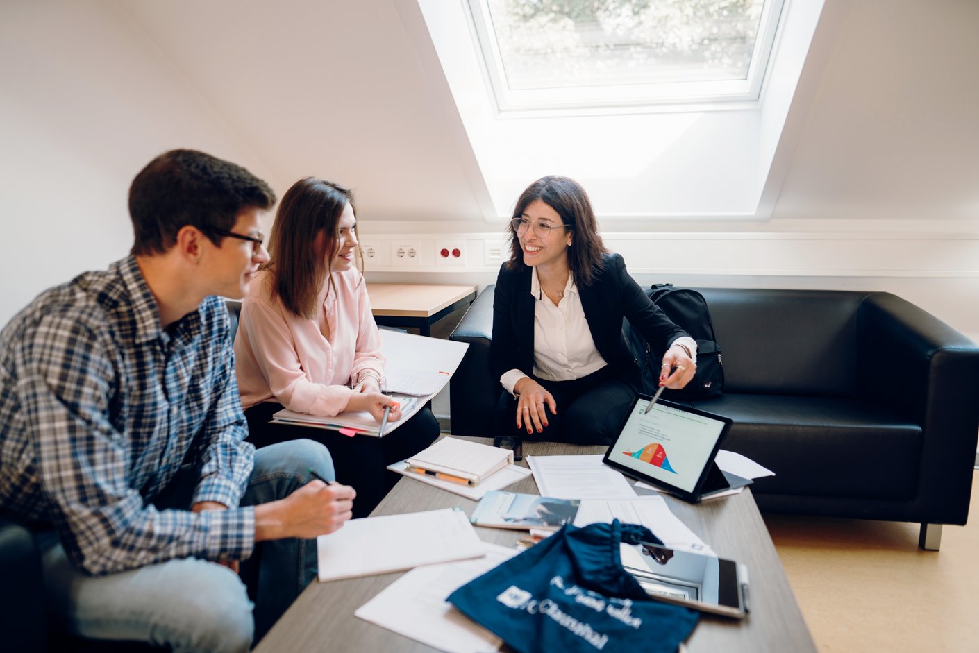 Eine Person erklärt zwei weiteren Personen eine Statistik am Bildschirm eines Tablets
