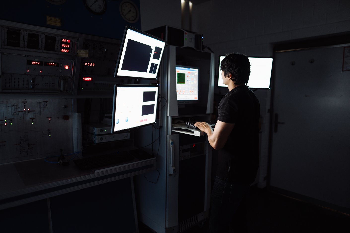 Eine Person arbeitet in einem dunklen Labor an einem Computer mit mehreren Bildschirmen