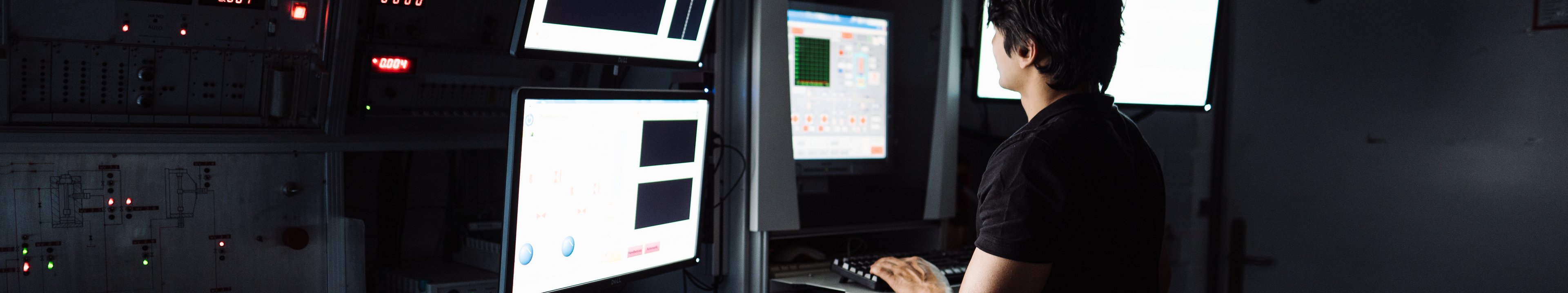 Eine Person arbeitet in einem dunklen Labor an einem Computer mit mehreren Bildschirmen