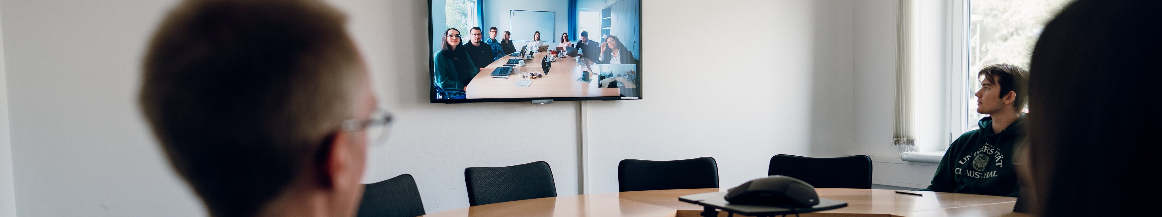 Studierende nehmen in einem Seminarraum an einer Videokonferenz teil.